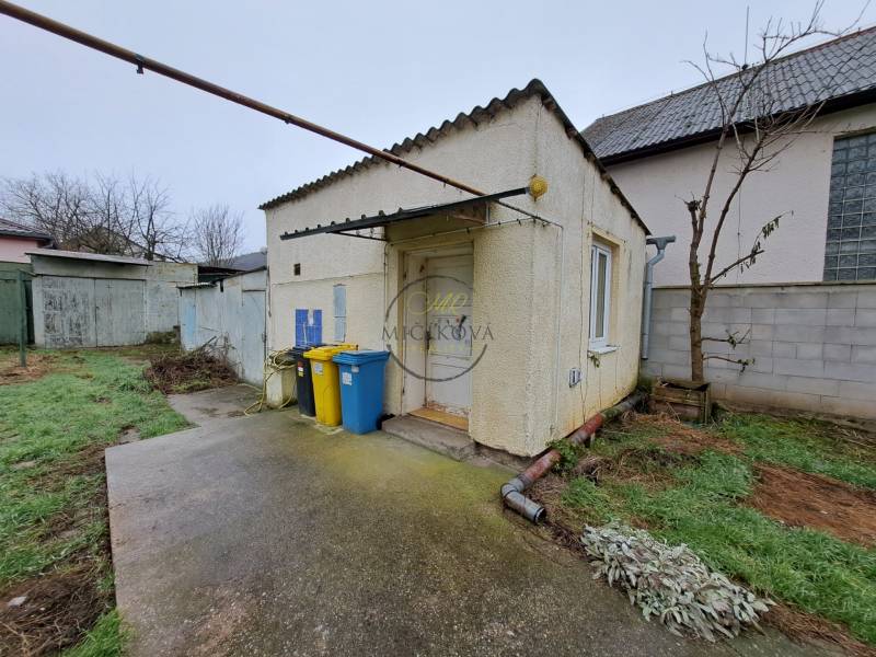 A family house on Mechenická Street in Podhorany with a concrete walkway, containers, and grass.