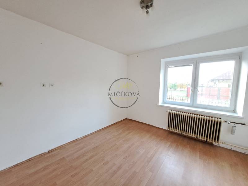 A room in a family house with white walls, a wood-patterned floor, and a large window.
