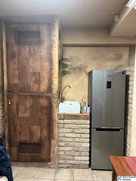 Rustic wall, next to a refrigerator and sink in commercial premises with wood-patterned flooring.
