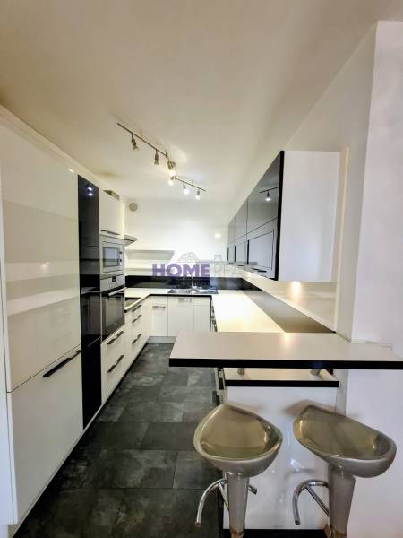 A kitchen in a 3-room apartment with bar stools, black and white cabinets.