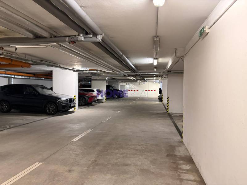 Underground garage with parking spaces, concrete walls, and lighting.
