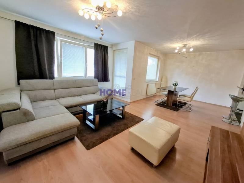 Living room in a 3-room apartment with a wooden decor floor, light furniture, and a large sofa.