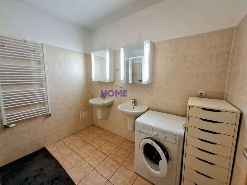 A bathroom in a 3-room apartment with mirrors, a washing machine, sinks, and light-colored tiles.