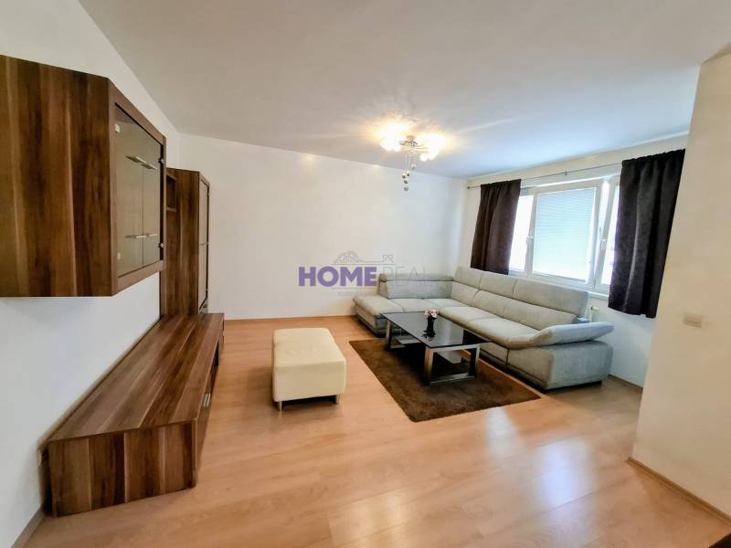 Living room in a 3-room apartment with a wooden decor floor, gray sofa, and furniture.