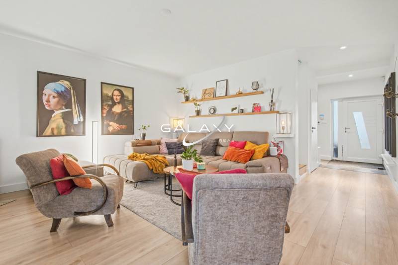 Living room of a family house with comfortable seating, decorative paintings, and a wooden-patterned floor.