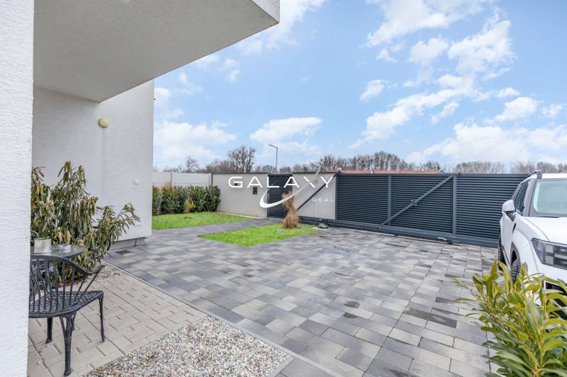 Courtyard of a family house in Dunajský Klátov, paving, greenery, modern fence, and parked car.