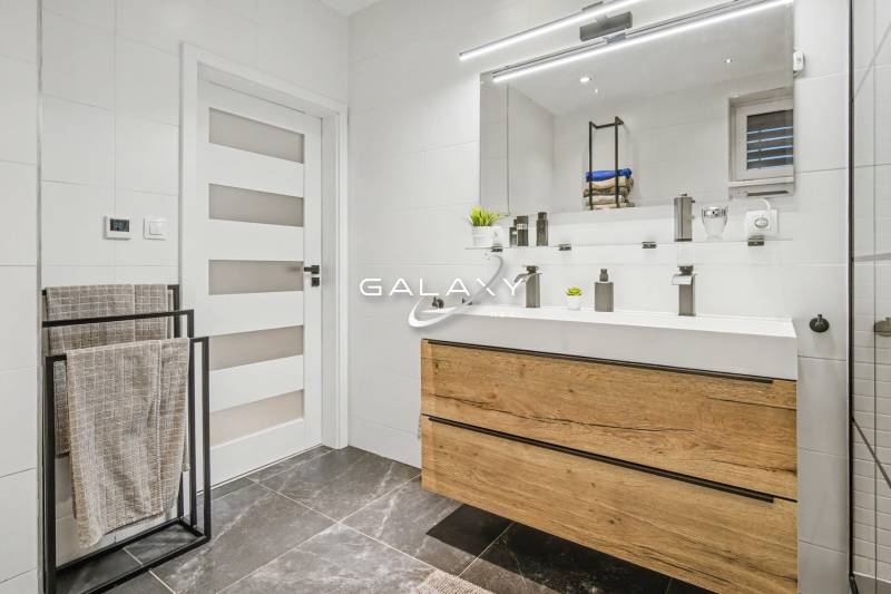 A bathroom in a family house with a dark stone floor, wooden decor of the cabinet under the sink.