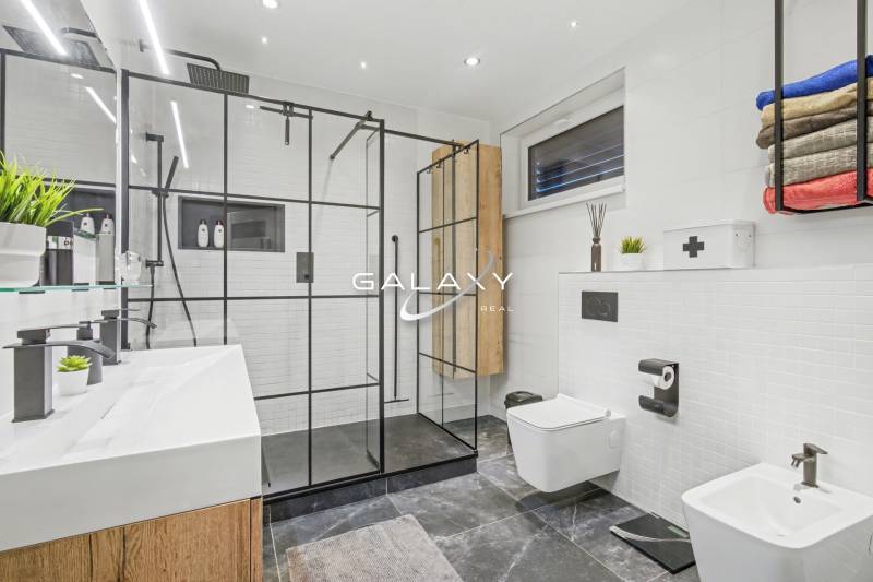 A bathroom in a family house with a glass shower enclosure, double sink, and white tiles.