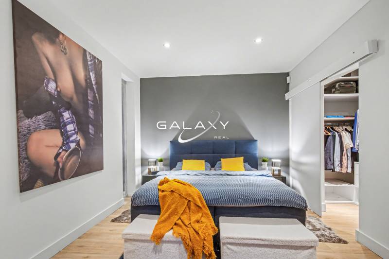 Bedroom in a family house with a bed, colorful pillows, and an open wardrobe.