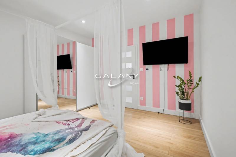 Bedroom in a family house with a striped wall, television, and wood-patterned flooring.