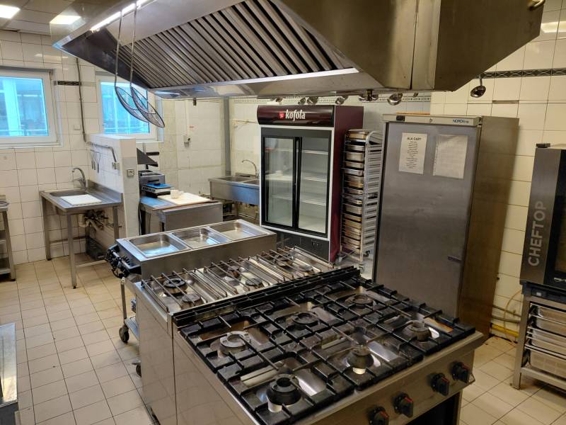 A kitchen in a gastro space with a stove, sink, and refrigeration equipment.