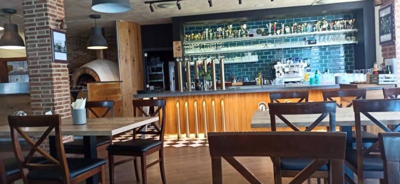 A café with a wooden decor floor, a bar counter, and brick elements in the gastro area.