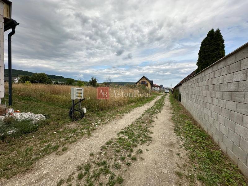 A dirt road surrounded by grassy residential plots on Poľnohospodárska Street in Trenčín.