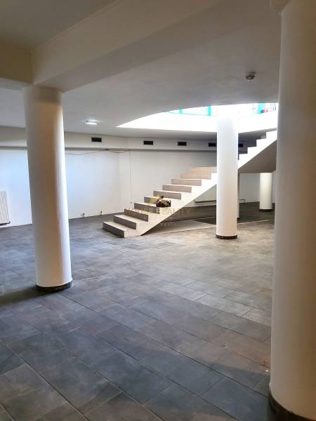 Commercial spaces with marble flooring and staircase, supported by columns.