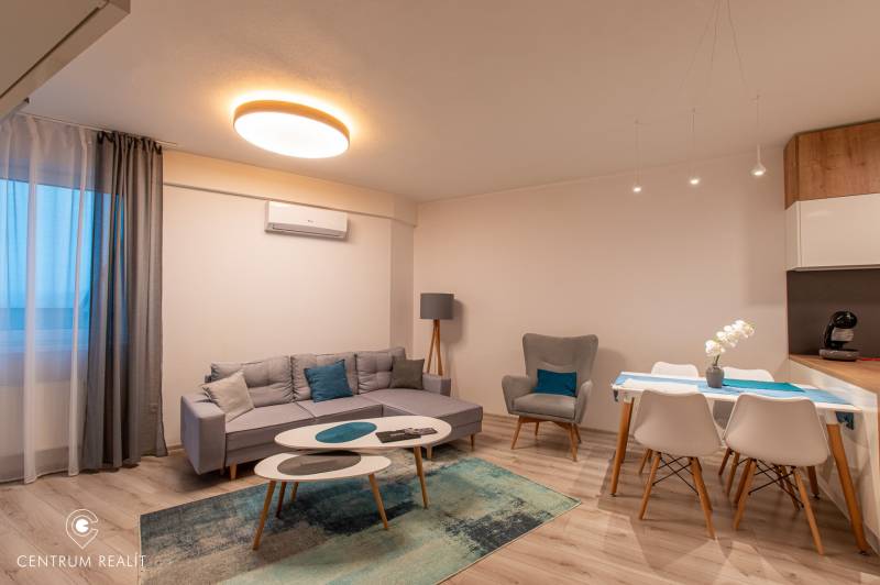 Living room in a two-room apartment with a wooden decor floor, a sofa, and a dining table.