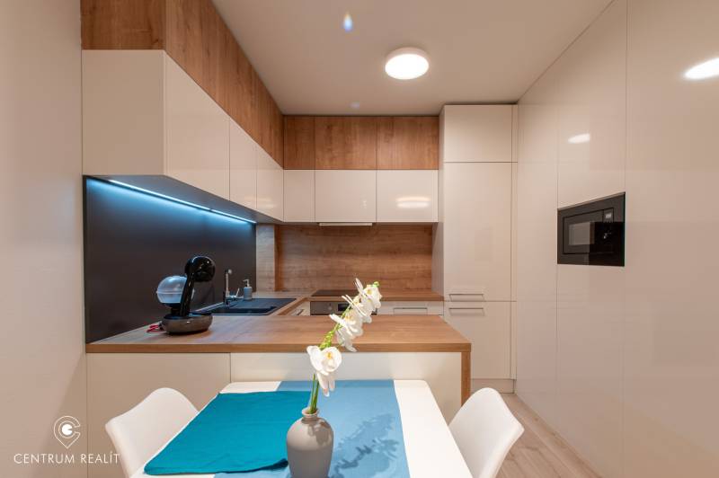 A kitchen in a 2-room apartment with light furniture and a wooden decor floor.