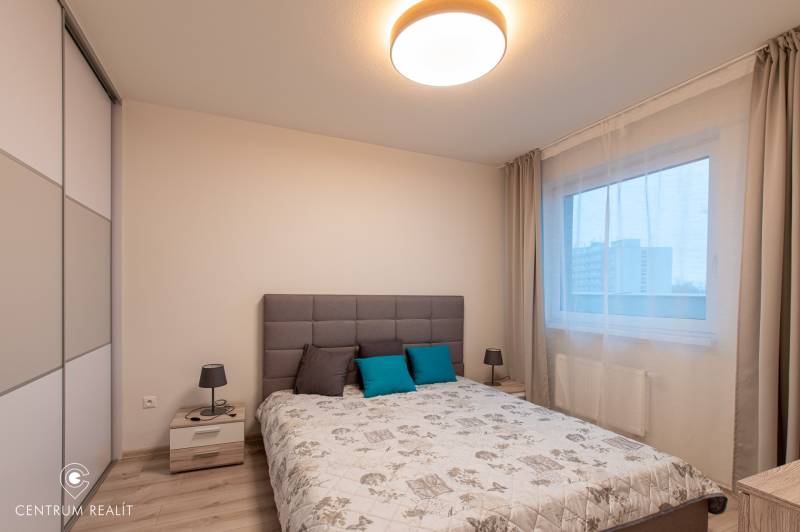 Bright bedroom with a bed, table, lamp, and wardrobe; floor with wood decor.