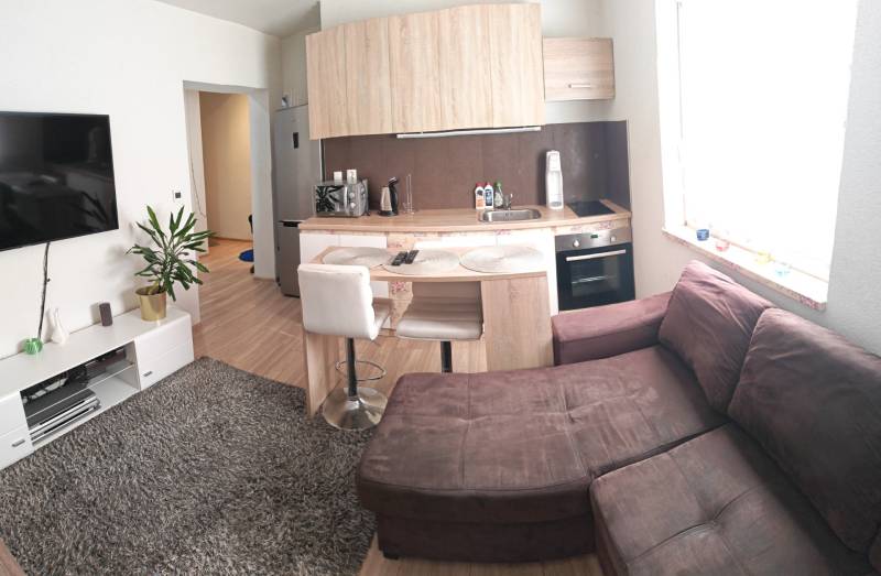 1-bedroom apartment with a kitchenette, sofa, TV, and wooden-style flooring.