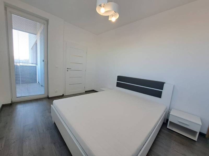 A bright bedroom in a two-room apartment with white furniture and a wooden decor floor.