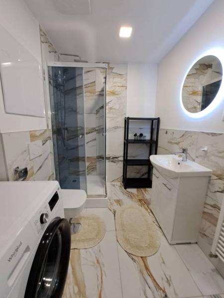 Bathroom in a 2-room apartment with a shower, washing machine, and oval mirror.