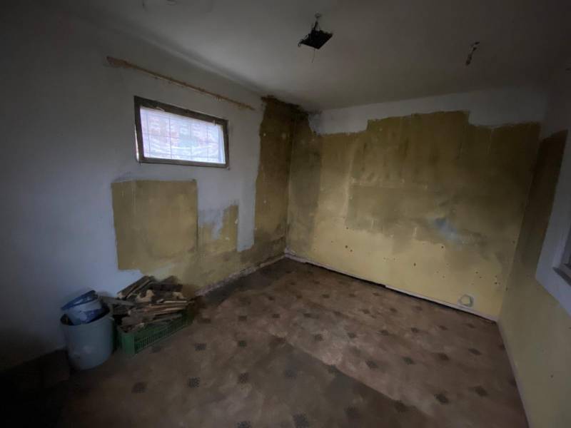 The interior of a cabin with raw walls and floor; building materials in the corner.