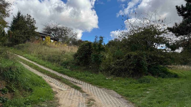 A cottage in Hlohovec, surrounded by nature and green bushes, with a visible dirt road.
