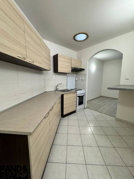 A kitchenette in a studio apartment with tiled flooring and light-colored cabinets, next to a floor with a wooden decor.