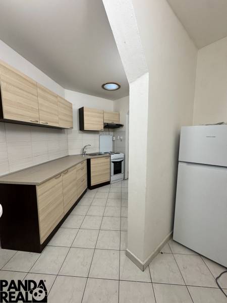 Kitchen area of a studio apartment with storage space and appliances, tiled floor, light shades.
