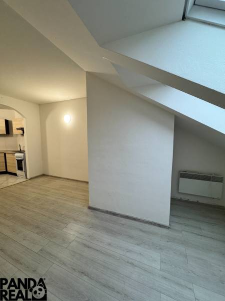 A studio apartment with a wooden floor, a kitchen, and a slanted ceiling.