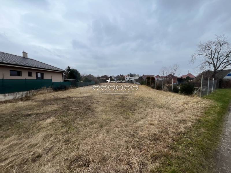 Building plot for housing in Hlohovec, grassy area between houses under a cloudy sky.