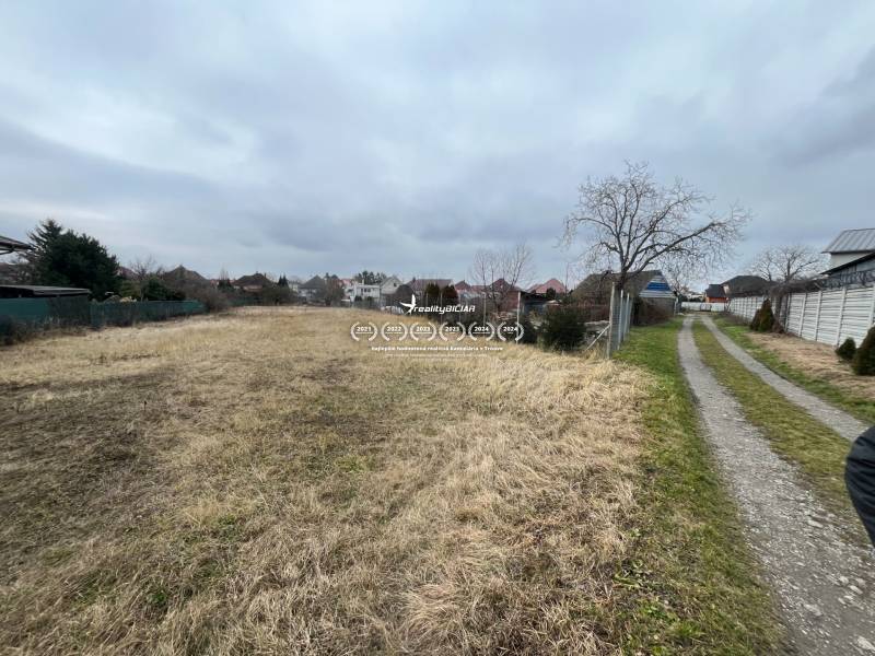 Land for sale on Ladislava Novomeského Street in Hlohovec, surrounded by family houses.