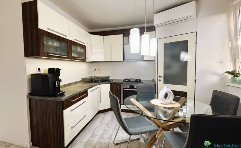 A kitchen in a 3-room apartment with modern furniture, a glass table, and a floor with a wood decor.