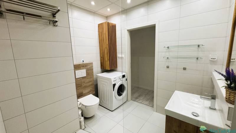A bathroom in a 3-room apartment with a washing machine, light tiles, and a decorative wooden element.