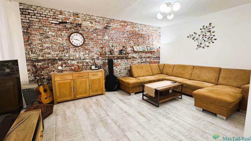 Living room in a three-room apartment with a brick wall, beige sofa, and wooden decor flooring.