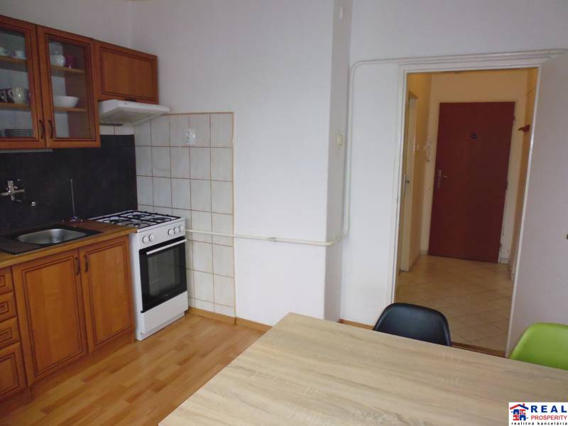 A kitchen in a studio apartment with a simple kitchenette and a floor with a wood decor.