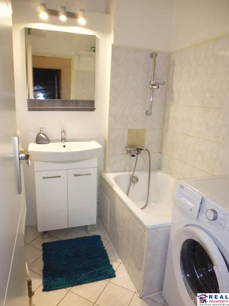Bathroom in a studio apartment with a bathtub, sink, mirror, and washing machine.