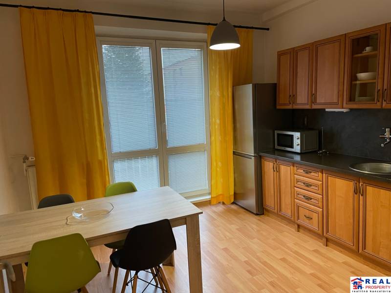 A kitchen in a studio apartment with yellow curtains and a wood-patterned floor.