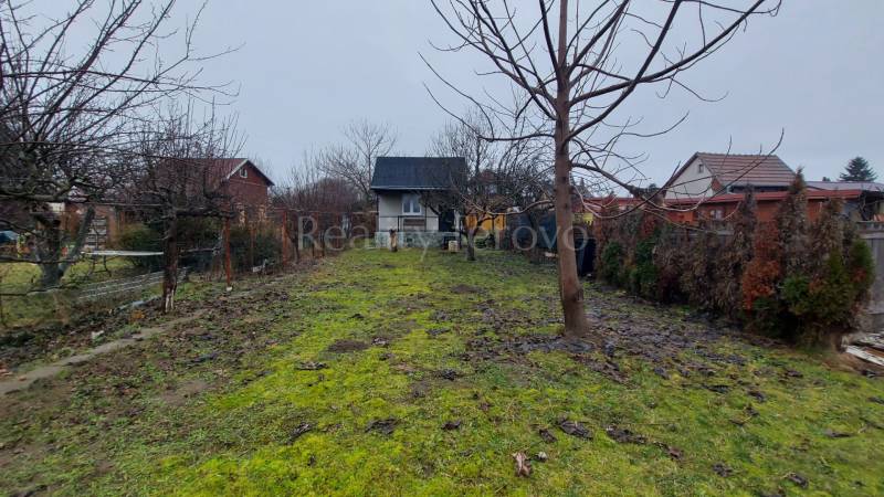 A garden with a cottage in Nové Zámky surrounded by trees and a grassy area.