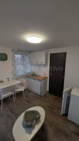 A cottage with a kitchenette, a table, white cabinets, and a floor with a wood decor.