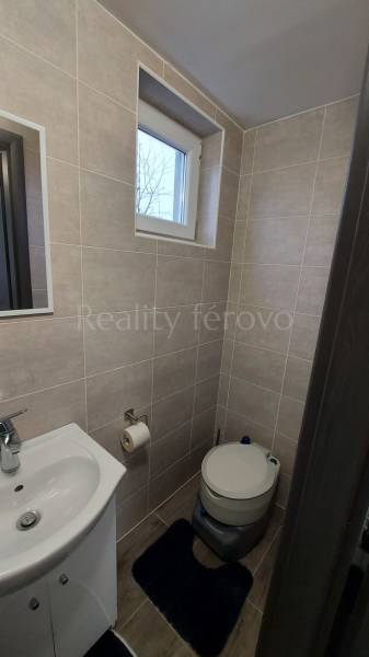 A bathroom in a cottage with a sink, toilet, and window, tiled with light tiles.