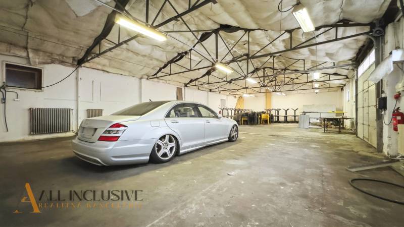 Interior of commercial space with a car, exposed ceiling, tables, and chairs.