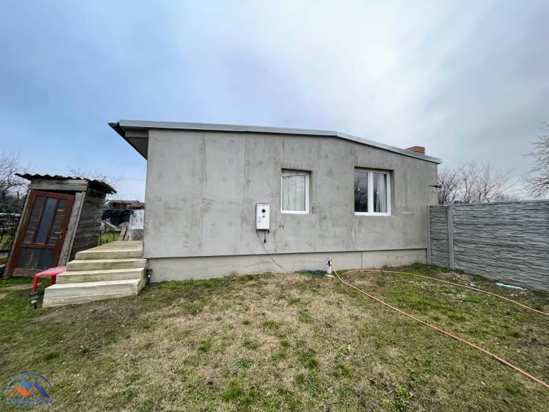 A cottage in Komárno with a concrete facade, stairs, and a fenced plot.