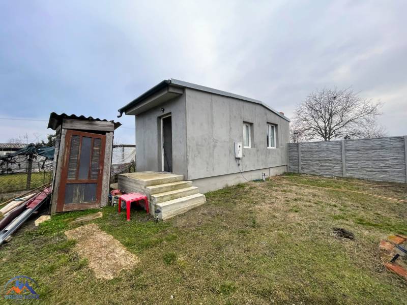 A house in Komárno with a concrete facade, a staircase, and a garden surrounded by a fence.