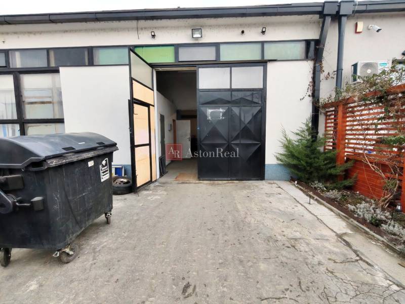 An industrial gate leads to the Warehouses and Halls in Trenčín. There is a garbage bin outside.