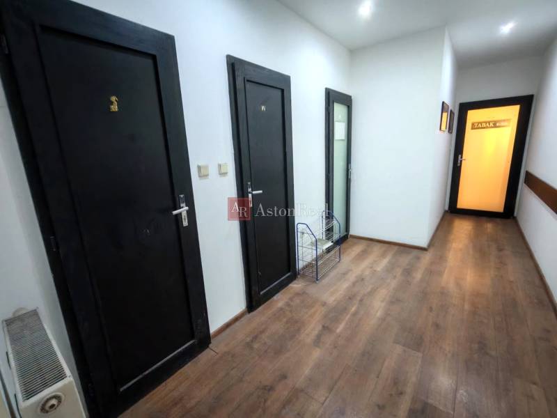 A corridor in a warehouse and hall with a wooden decor floor and black doors.