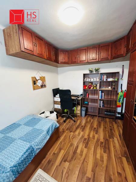 A room in a 3-room apartment contains a bed, a shelf, a desk, and a floor with a wooden decor.