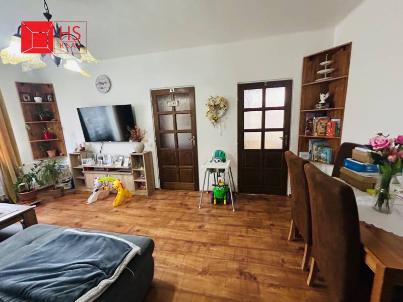 Living room with a sofa, wooden decor flooring, a television, and children's toys in a three-room apartment.