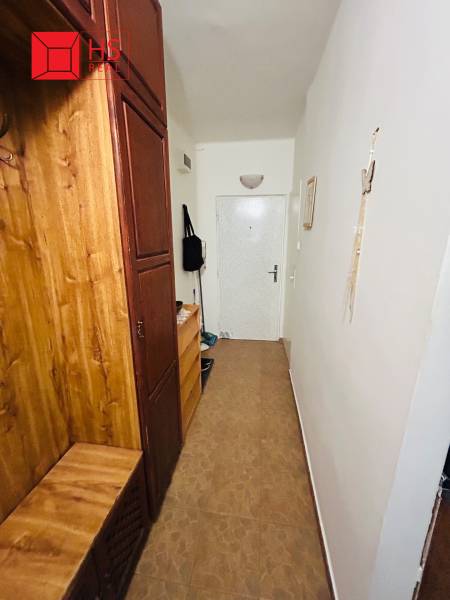 A narrow hallway with wooden furniture and white walls in a 3-room apartment.
