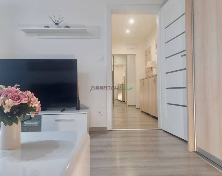Living room in a two-room apartment with a television, flowers, and a wooden decor floor.