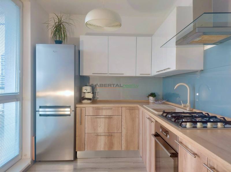 A kitchen in a 2-room apartment with a wooden decor floor, light cabinets, and a stainless steel refrigerator.